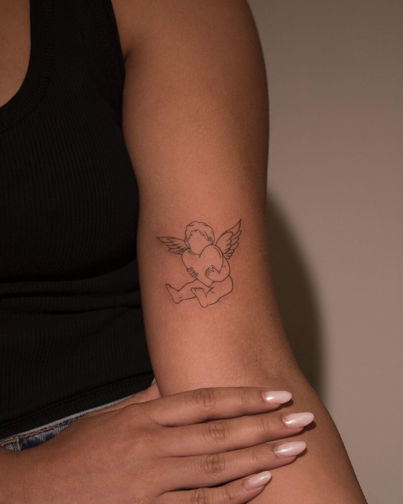 Angel holding a heart with wings on the chest tattoo above the elbow: divine love guardian 