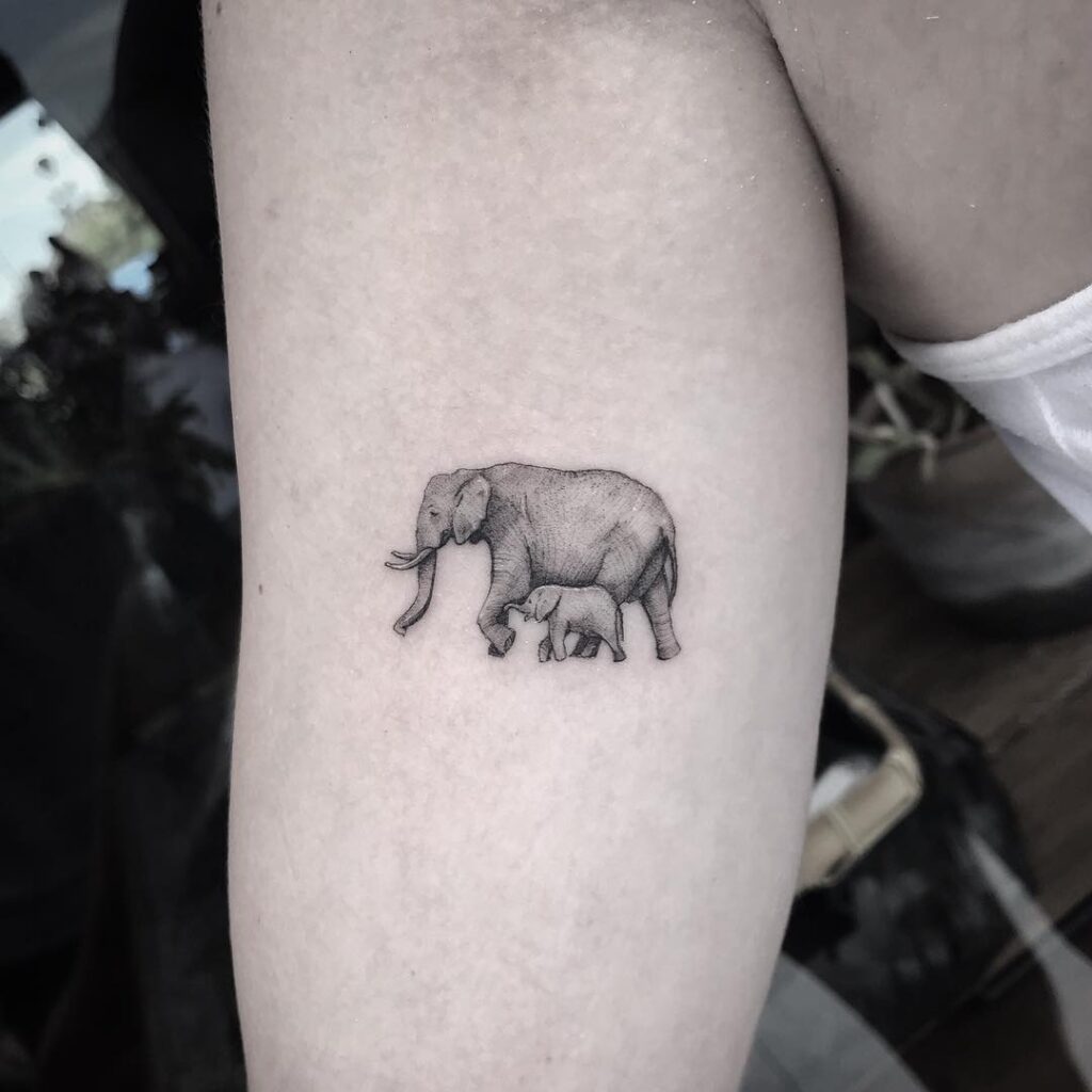 Black and grey mom and baby elephant tattoo on bicep, walking together in realistic detail maternal grace 