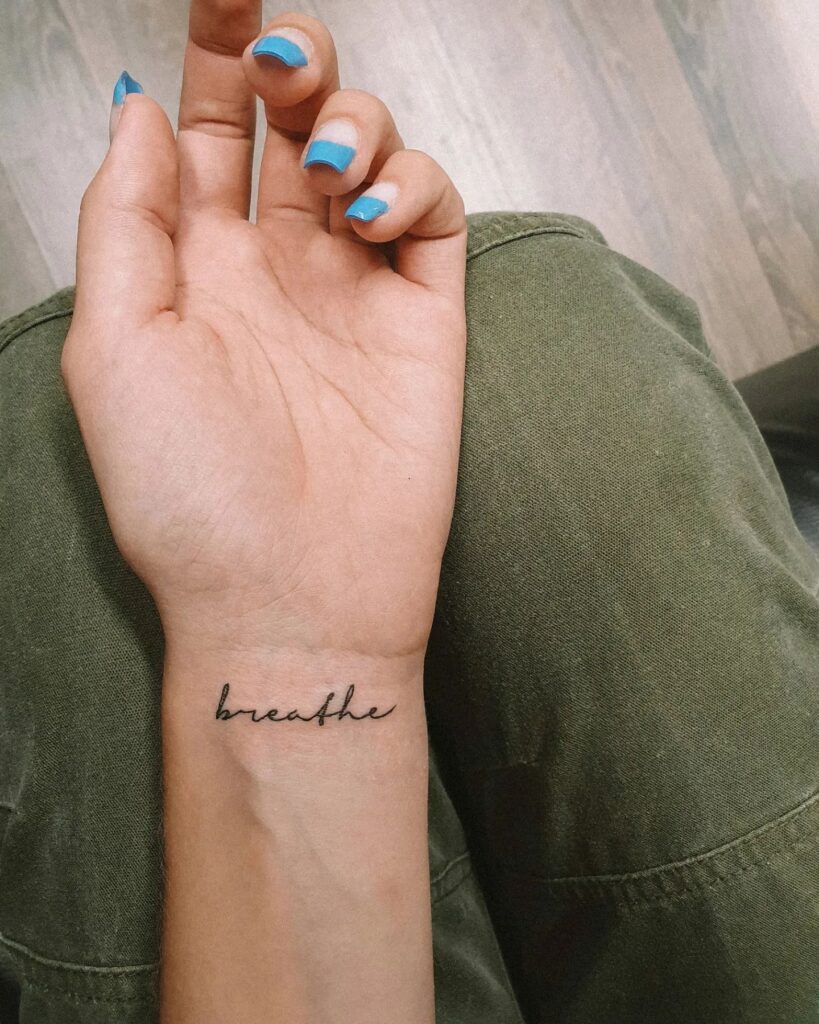 Breathe word script lettering tattoo on the inner wrist, showcasing thin font weight for a stylish reminder: breathe easy 