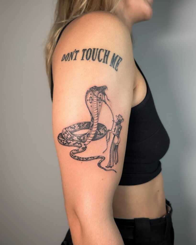 Cowgirl's command snake control with 'don't touch me' lettering upper arm tattoo 