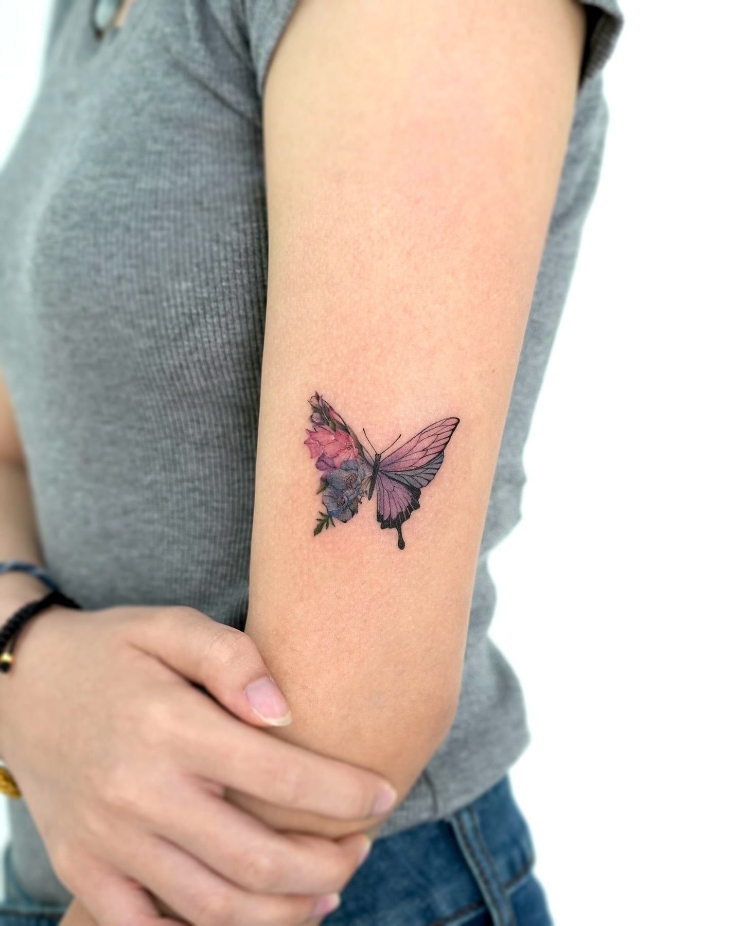 Floral butterfly tattoo with pink and purple ink on outer arm 
