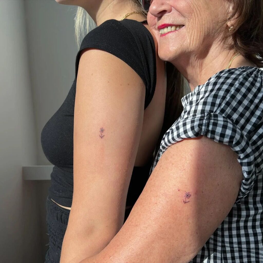 Mother-daughter bond matching small flower tattoos on the upper arm 