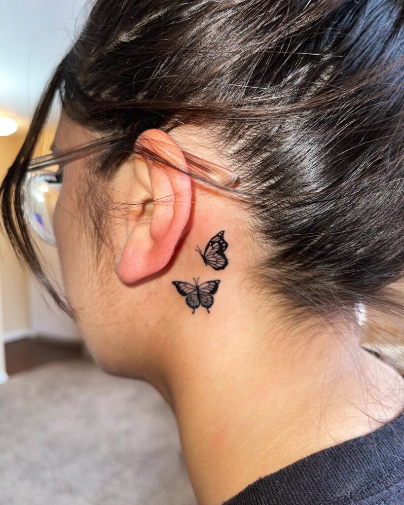 Simple beauty in motion two moving black butterflies behind the ear tattoo 