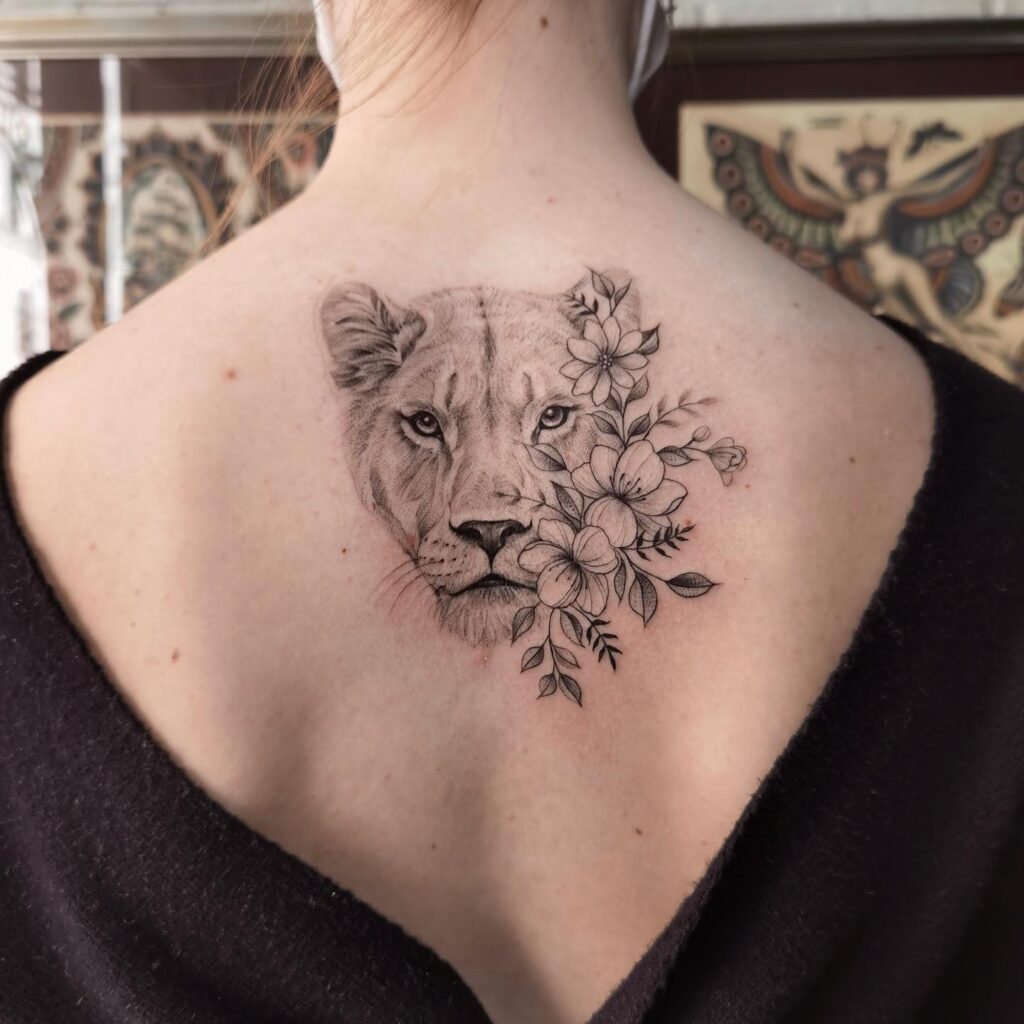Simple lioness with florals tattoo on the back: feline femininity 