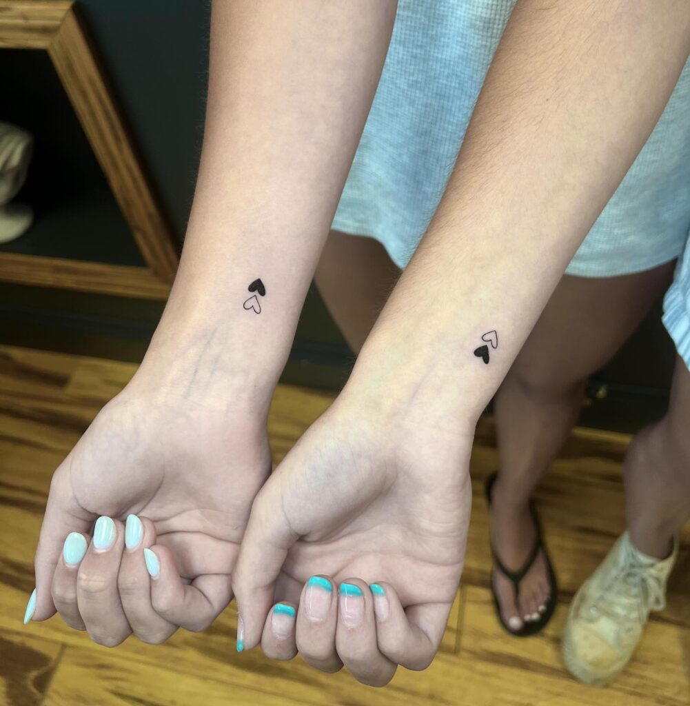 Sisters matching heart tattoos one filled one outline on wrists 