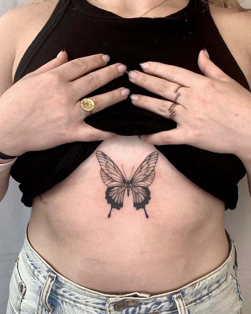 Symmetrical butterfly sternum tattoo with fine-line details and shading 