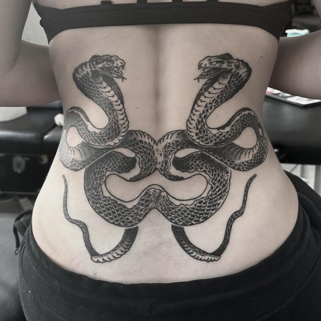 Symmetrical lower back cobra tattoo in black work: angry elegance 