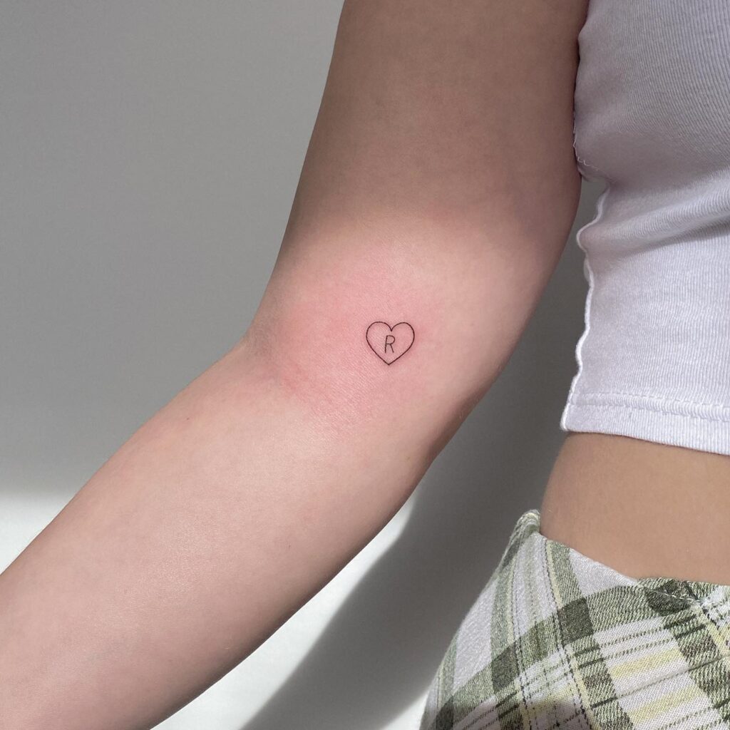 Tiny outline heart tattoo located on the inner arm with r letter inside the heart 